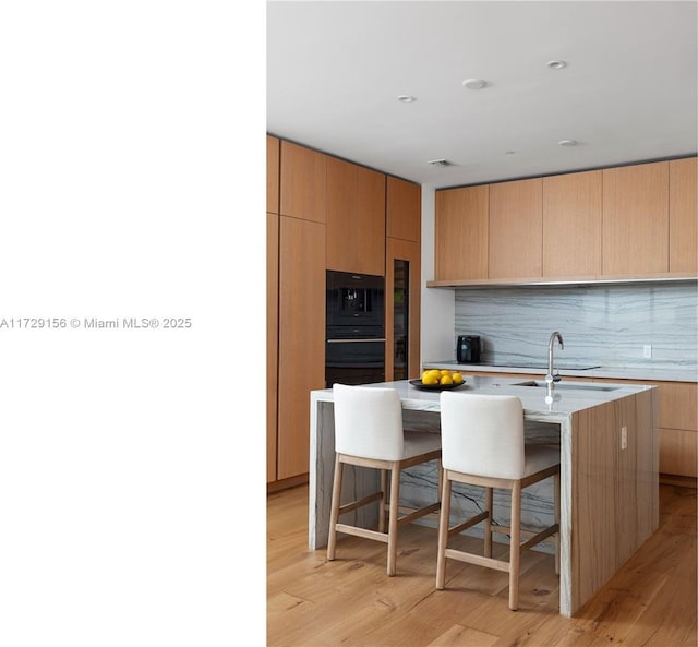 kitchen with a kitchen bar, sink, light hardwood / wood-style flooring, a kitchen island with sink, and decorative backsplash