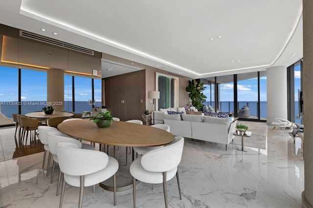 dining space with a wall of windows, a raised ceiling, and a water view