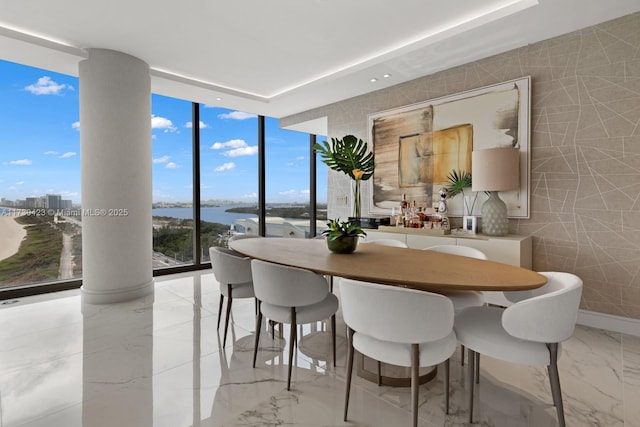 dining room featuring a water view, floor to ceiling windows, tile walls, and ornate columns