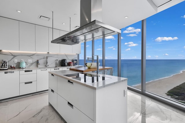 kitchen featuring a water view, tasteful backsplash, island range hood, white cabinets, and a kitchen island