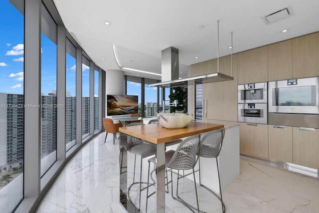 kitchen with light brown cabinetry, a breakfast bar area, decorative light fixtures, double oven, and expansive windows