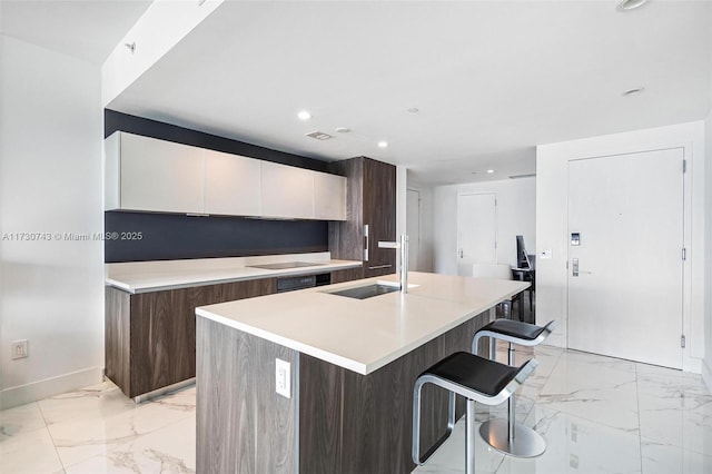 kitchen featuring dark brown cabinetry, white cabinetry, sink, a kitchen island with sink, and a breakfast bar area