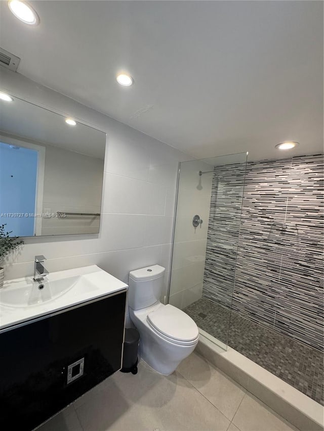 bathroom featuring tile walls, vanity, a tile shower, tile patterned floors, and toilet