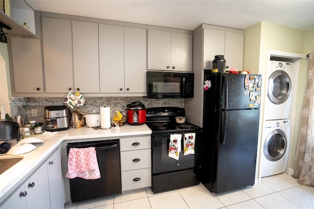 kitchen featuring black appliances, a textured ceiling, tasteful backsplash, stacked washing maching and dryer, and light tile patterned flooring