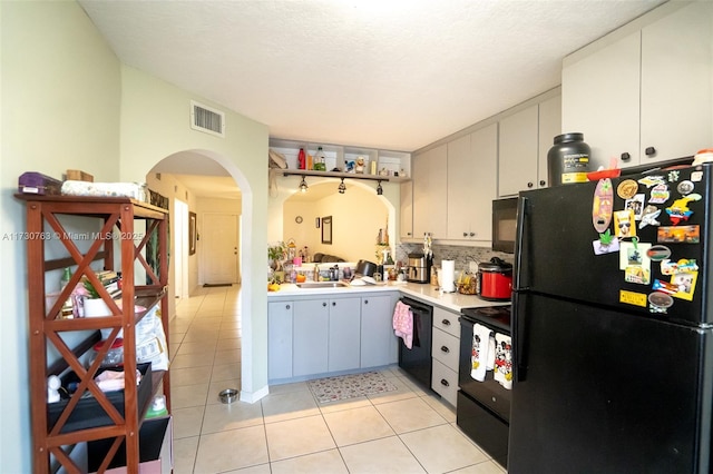 kitchen with sink, backsplash, white cabinetry, light tile patterned floors, and black appliances