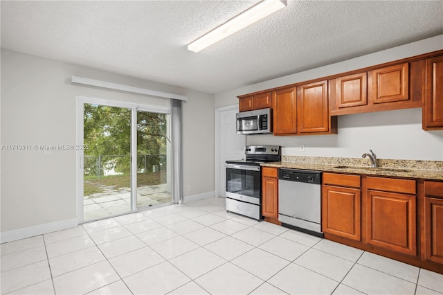 kitchen featuring light stone countertops, appliances with stainless steel finishes, a textured ceiling, light tile patterned floors, and sink