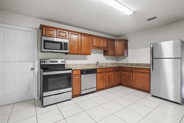 kitchen featuring light tile patterned floors, light stone countertops, a textured ceiling, and appliances with stainless steel finishes