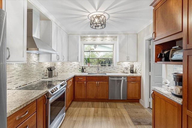 kitchen featuring wall chimney exhaust hood, sink, white cabinets, light stone counters, and stainless steel appliances