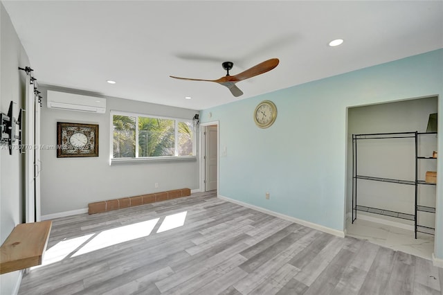 unfurnished bedroom with ceiling fan, a wall mounted air conditioner, and light wood-type flooring