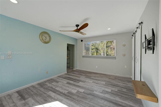 empty room with light hardwood / wood-style floors, a barn door, and ceiling fan