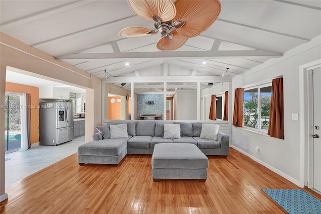 living room featuring ceiling fan, light hardwood / wood-style floors, and vaulted ceiling with beams