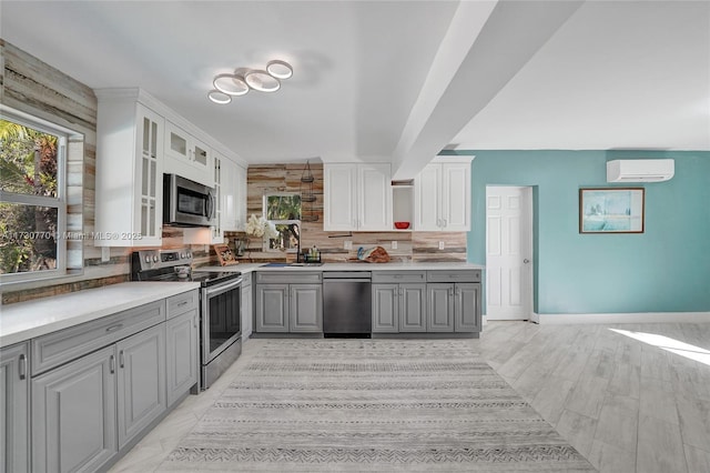 kitchen featuring appliances with stainless steel finishes, white cabinetry, gray cabinetry, tasteful backsplash, and an AC wall unit