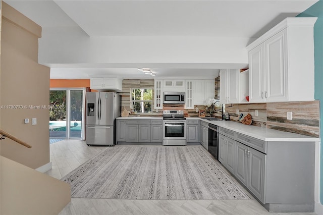 kitchen featuring sink, gray cabinetry, white cabinetry, tasteful backsplash, and appliances with stainless steel finishes