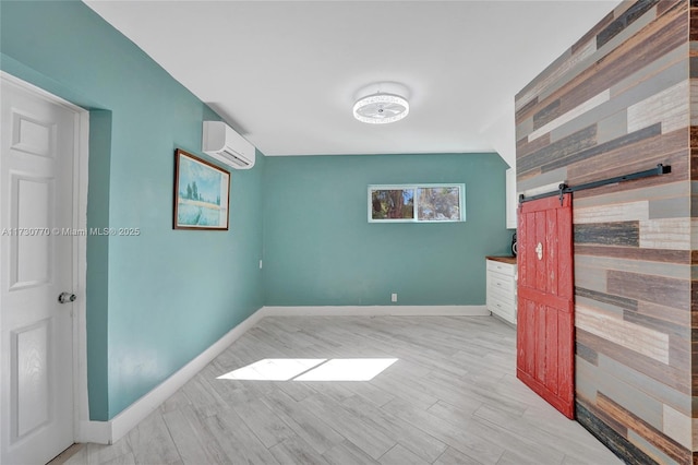 unfurnished room with a wall mounted air conditioner, a barn door, and light wood-type flooring