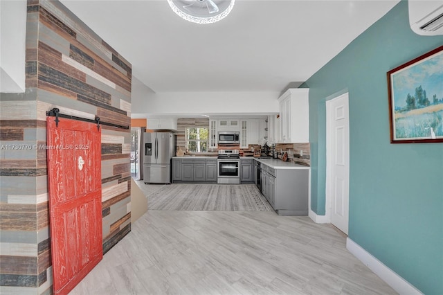 kitchen with appliances with stainless steel finishes, gray cabinetry, a wall mounted air conditioner, white cabinets, and a barn door