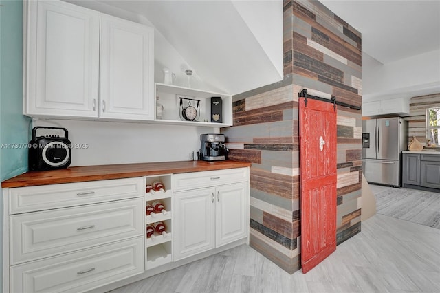 kitchen with butcher block counters, stainless steel fridge with ice dispenser, white cabinetry, and a barn door