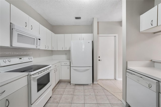 kitchen with light tile patterned flooring, a textured ceiling, white cabinets, and white appliances