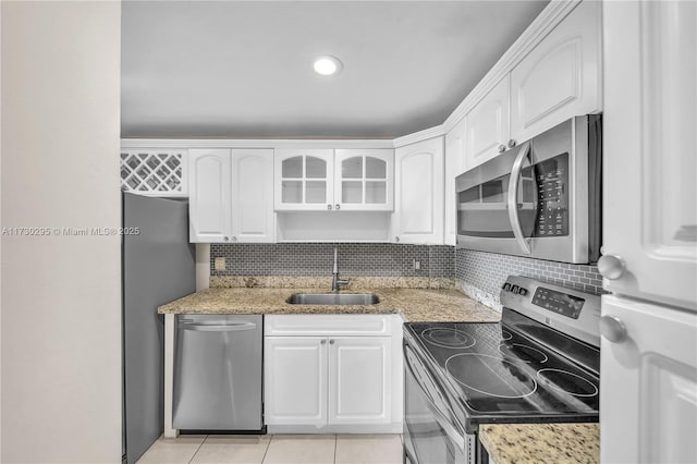 kitchen with appliances with stainless steel finishes, light tile patterned floors, sink, white cabinets, and light stone counters