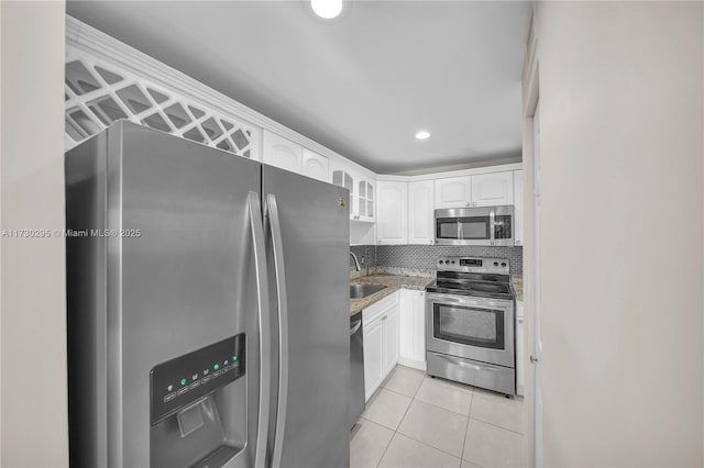 kitchen with appliances with stainless steel finishes, white cabinetry, light tile patterned floors, sink, and stone countertops