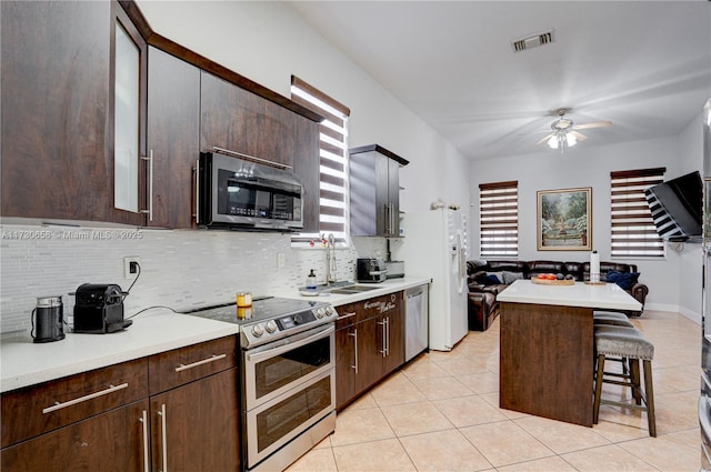 kitchen with dark brown cabinetry, stainless steel appliances, decorative backsplash, a kitchen breakfast bar, and sink