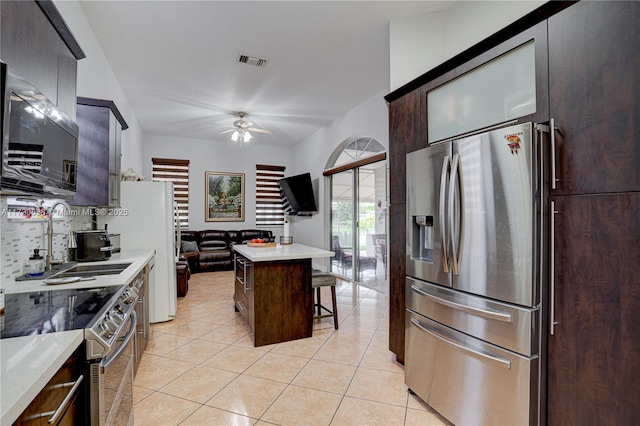 kitchen with appliances with stainless steel finishes, sink, light tile patterned flooring, a breakfast bar, and a kitchen island