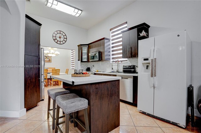 kitchen with dark brown cabinets, appliances with stainless steel finishes, sink, light tile patterned floors, and a center island