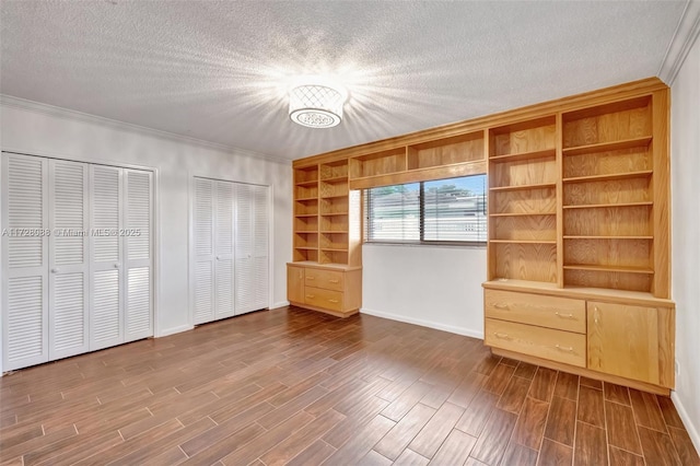 unfurnished bedroom with an inviting chandelier, a textured ceiling, crown molding, multiple closets, and wood finished floors