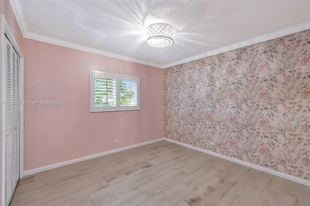 unfurnished room featuring wallpapered walls, wood finished floors, baseboards, and ornamental molding