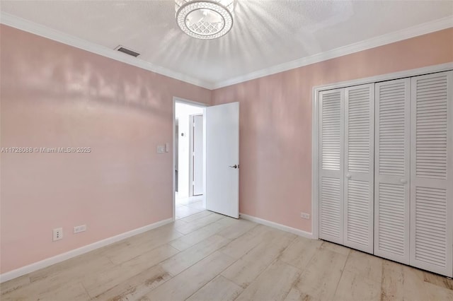 unfurnished bedroom with visible vents, baseboards, a closet, ornamental molding, and wood finished floors