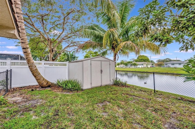 view of yard featuring a water view, a fenced backyard, an outbuilding, and a storage unit