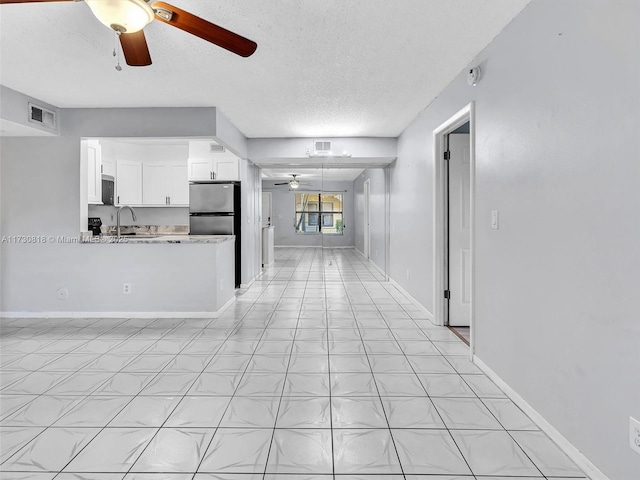 kitchen featuring stainless steel fridge, ceiling fan, sink, white cabinetry, and light stone counters