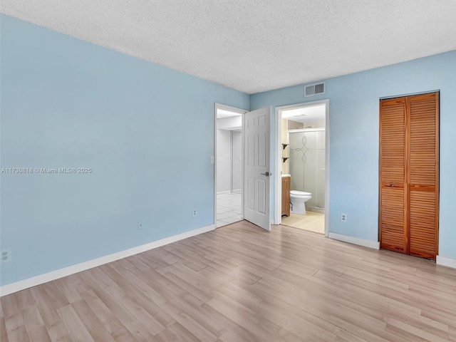 unfurnished bedroom with a textured ceiling, a closet, ensuite bath, and light wood-type flooring