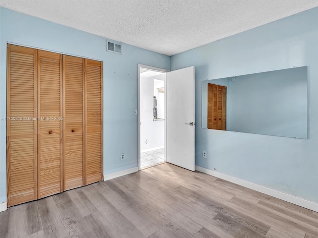 unfurnished bedroom featuring light hardwood / wood-style floors, a textured ceiling, and a closet