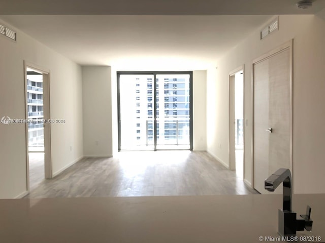 spare room with expansive windows and light hardwood / wood-style flooring