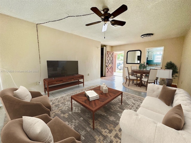 living room with ceiling fan, light tile patterned floors, and a textured ceiling