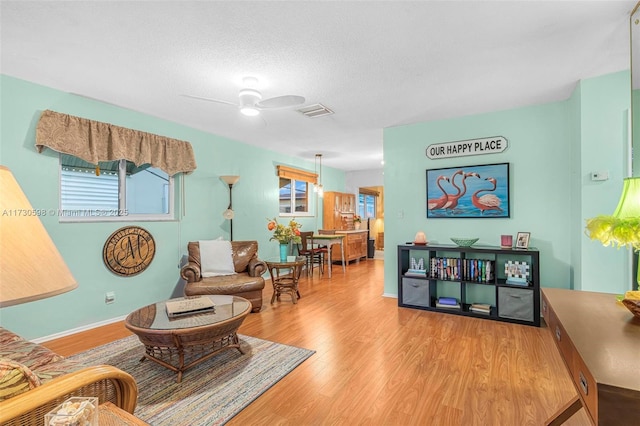 living area with ceiling fan, light hardwood / wood-style floors, and a textured ceiling