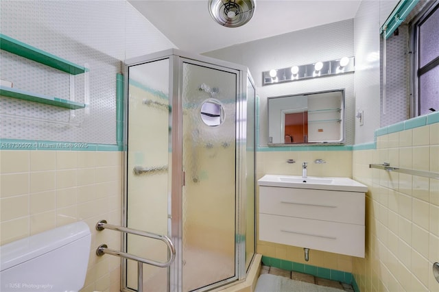 bathroom featuring a shower with door, vanity, tile walls, and toilet