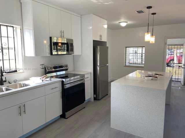 kitchen featuring hanging light fixtures, appliances with stainless steel finishes, sink, white cabinets, and a center island