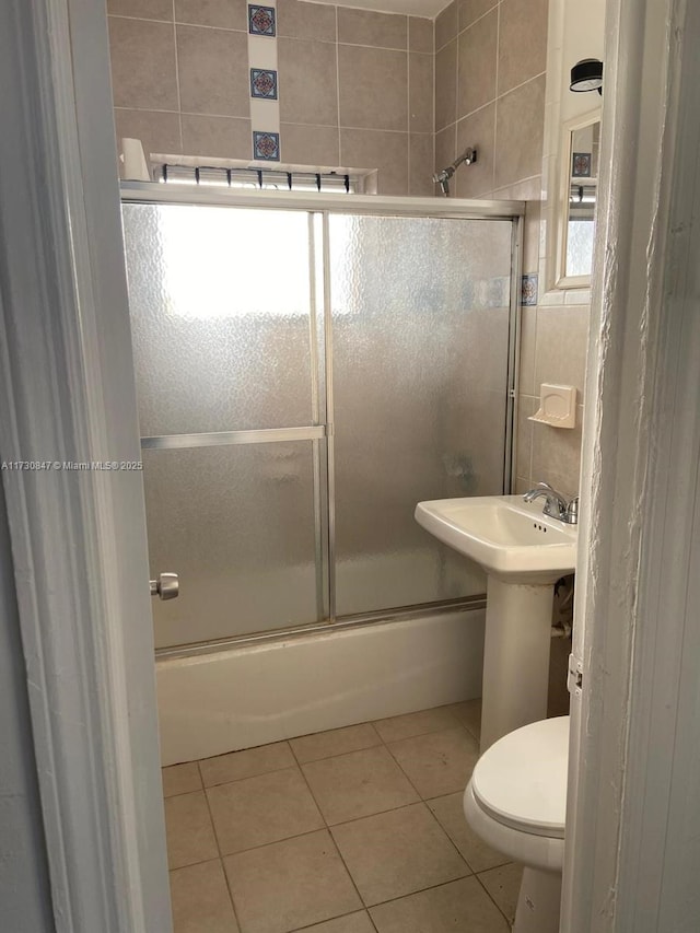 full bathroom featuring shower / bath combination with glass door, tile patterned floors, sink, tile walls, and toilet