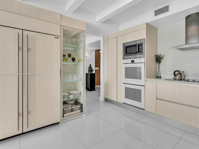 kitchen featuring light brown cabinets, stainless steel microwave, black electric stovetop, light tile patterned flooring, and wall chimney range hood