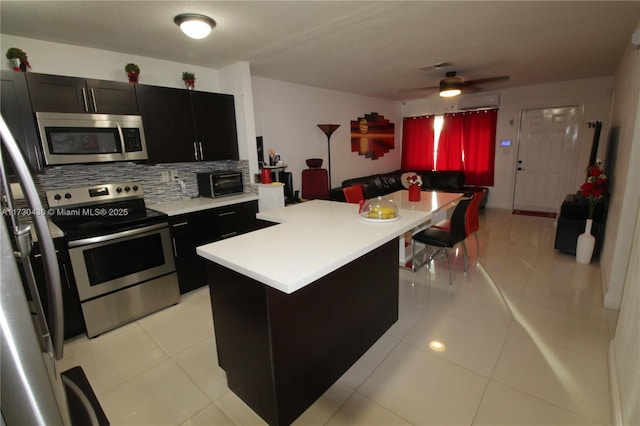 kitchen featuring ceiling fan, stainless steel appliances, a center island, light tile patterned flooring, and decorative backsplash