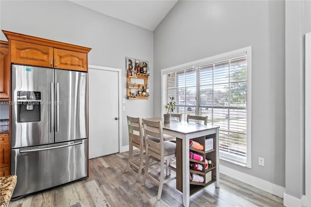 kitchen featuring high vaulted ceiling, light hardwood / wood-style flooring, and stainless steel fridge