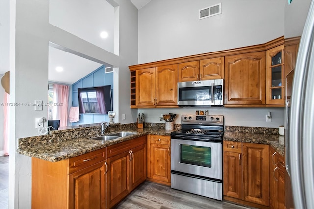 kitchen with sink, dark stone countertops, lofted ceiling, and appliances with stainless steel finishes