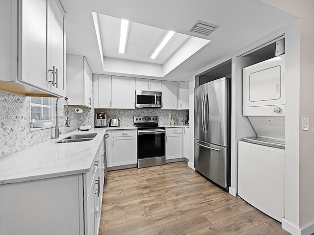 kitchen with light stone countertops, white cabinets, appliances with stainless steel finishes, sink, and stacked washer and clothes dryer