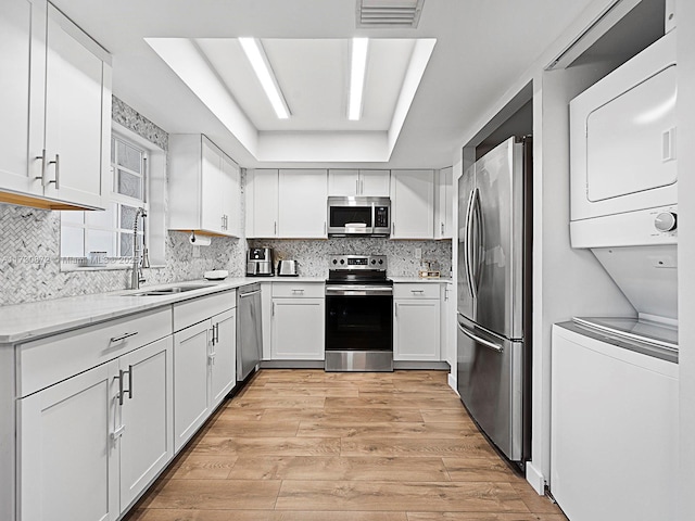 kitchen featuring sink, stainless steel appliances, white cabinetry, and stacked washer and dryer