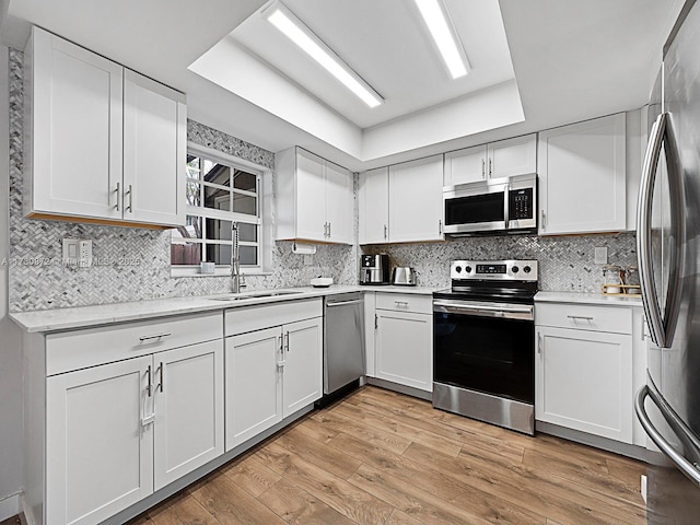 kitchen featuring a raised ceiling, sink, white cabinetry, light hardwood / wood-style floors, and stainless steel appliances