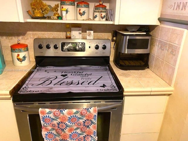 kitchen with white cabinetry, tile counters, decorative backsplash, and stainless steel electric range