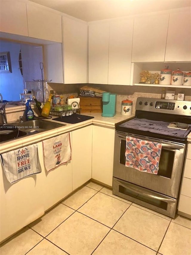 kitchen with light tile patterned flooring, white cabinets, sink, and electric range