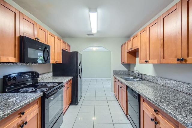 kitchen featuring sink, black appliances, light tile patterned floors, and dark stone countertops