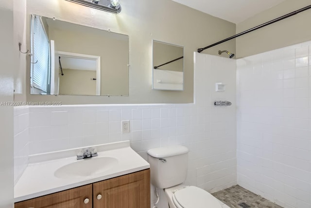 bathroom with vanity, toilet, tiled shower, and tile walls